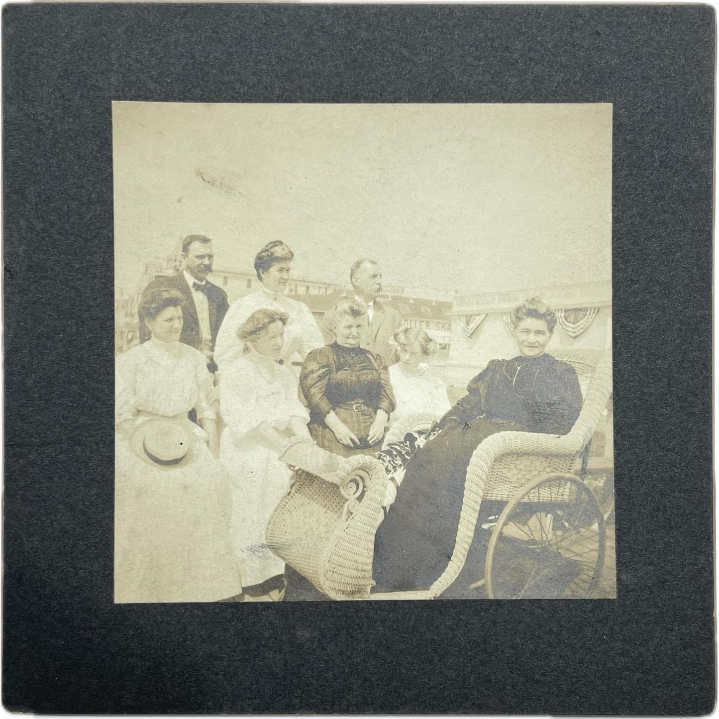 [Mounted photograph portrait of a family, including woman in wicker rolling chair]
